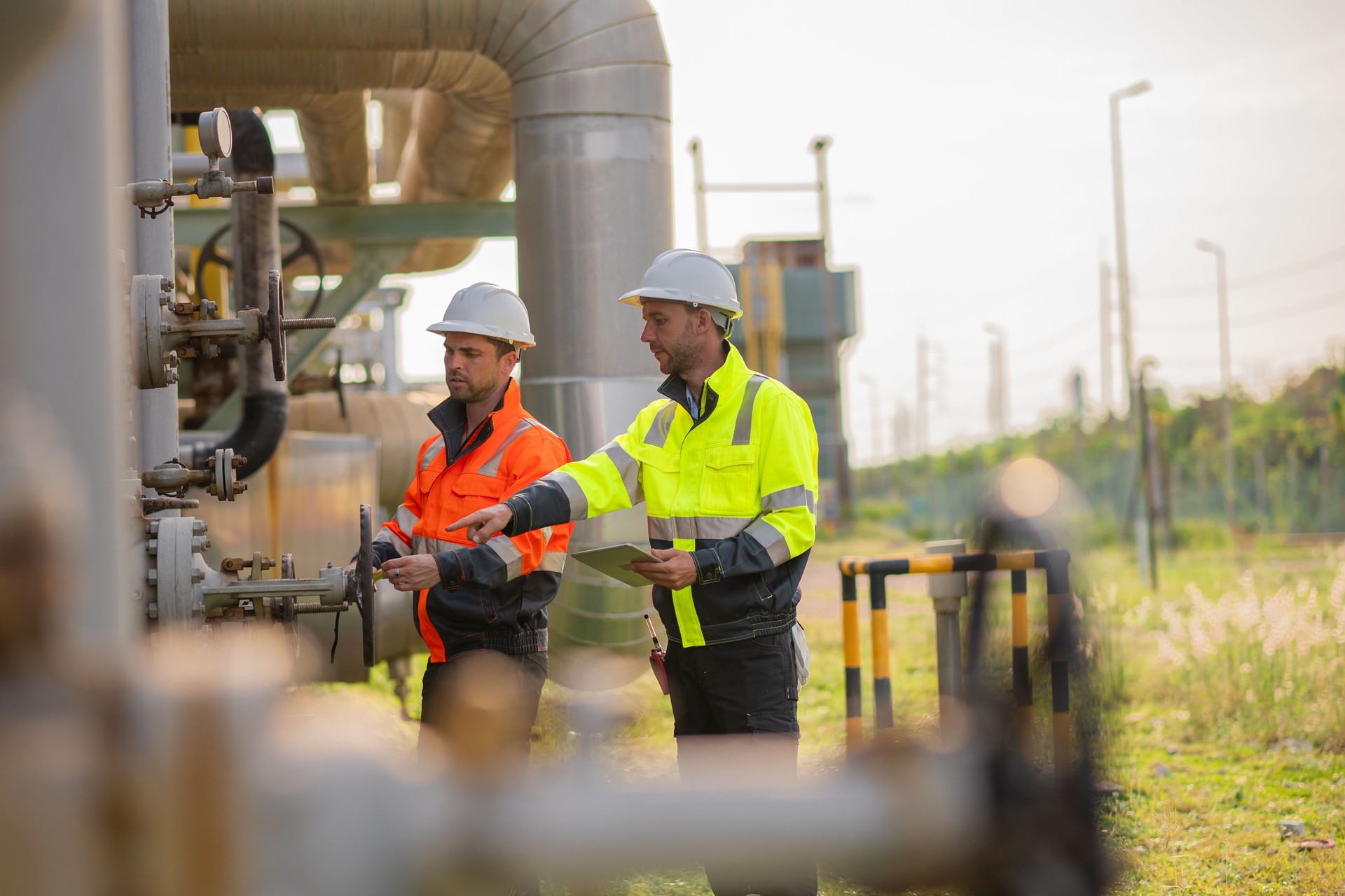 Engineers or industrial worker at large metal pipelines and valve systems oil refinery, chemical plant, or gas processing facility analyzing data is industrial safety, and operational efficiency.